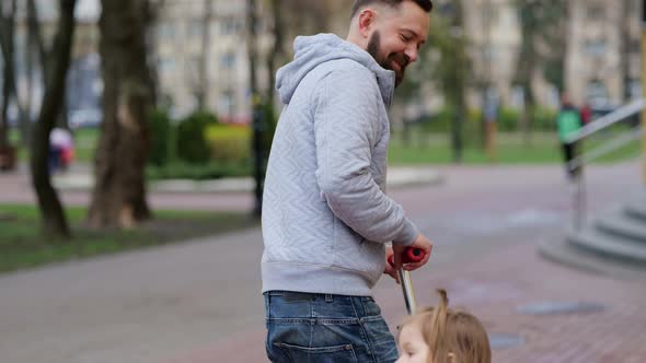 Father Taking Care of Little Girl While Riding Scooters in Park
