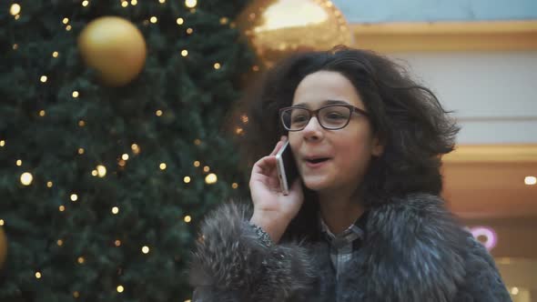 Happy Young Girl Talking on the Phone on the Background of the Christmas Tree