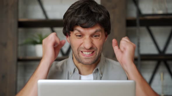 Happy Winner. Young Excited Man Using Laptop Computer While Sitting on Sofa. alt