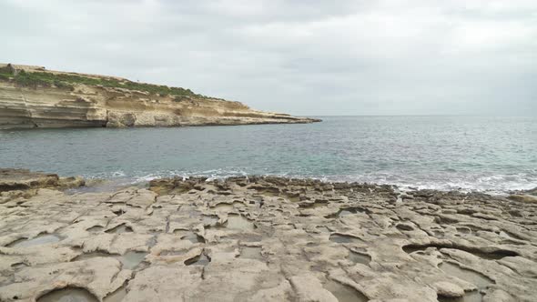 Limestone Beach Il-Kalanka in Malta with Holes in Ground Filled With Water on Cloudy Moody Day