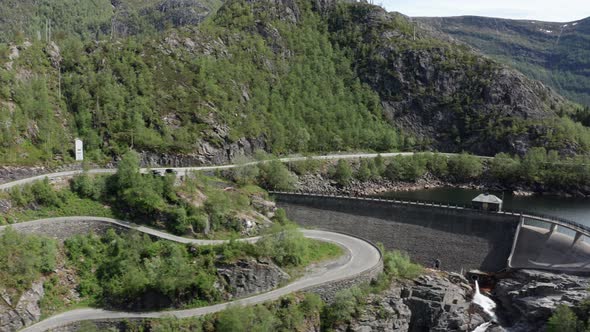 Aerial Flying backwards Reveal Small dam and winding Roads on the hill - Bergsdalen alt