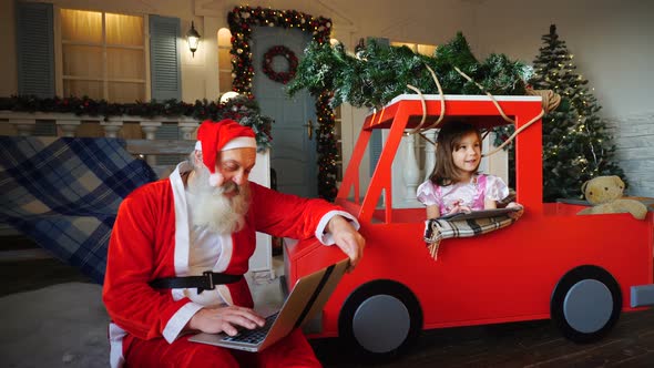 Joyous Santa Claus Satisfying with Laptop and Little Girl Playing on Tablet.