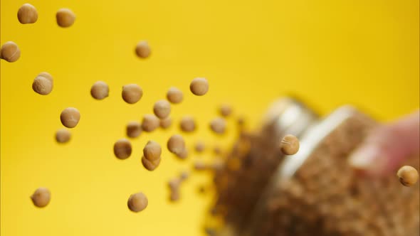 Closeup of Falling Down Chickpeas on Glass Table on Yellow Background alt