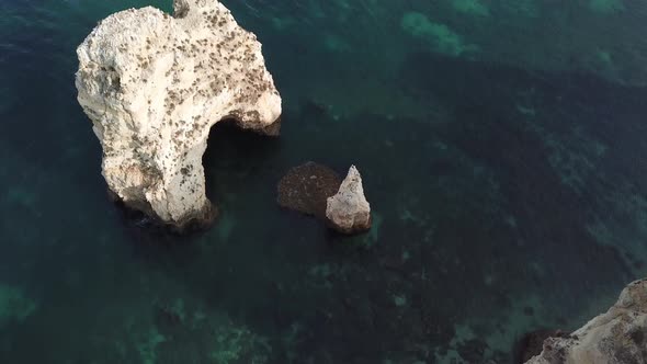 Tilting up to view calm sea and limestone cliffs along Algarve coastline, Portugal, aerial. alt