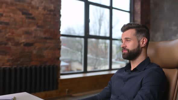 Side View of Smiling Young Businessman Waving at PC Webcam alt