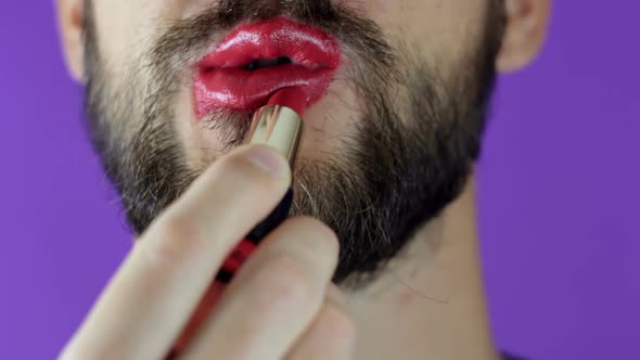 A Young Guy with a Beard Paints His Lips with Red Lipstick