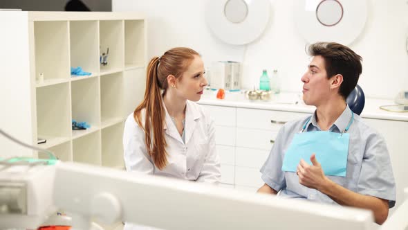 Young Empathic Female Dentist Listening to Male Patient Complaints During Dental Consultation alt