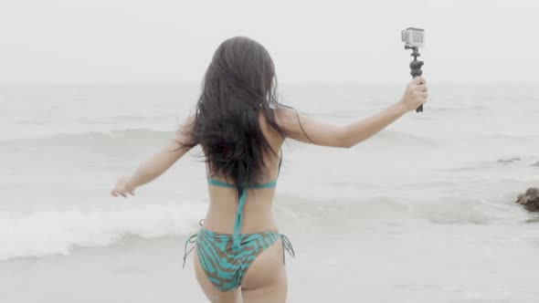 Beautiful young asian woman in bikini running and selfie with camera at beach. alt