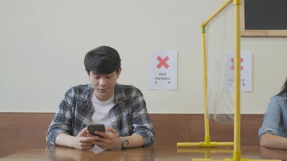 man and woman sitting in restaurant using phone and waitting food and keep distance alt