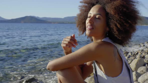 Slow motion shot of young smiling woman sitting on the beach alt