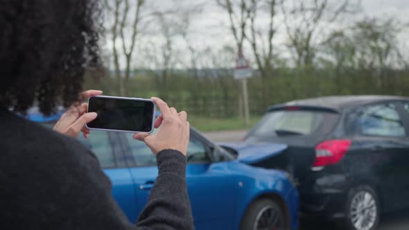 Rear view of female driver taking photos of road traffic accident on mobile
