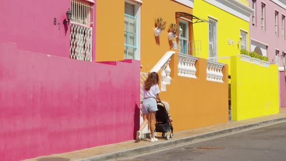 Woman Walking with Baby Stroller in the Streets of Colorful Buildings Neighbourhood BoKaap Cape Town alt