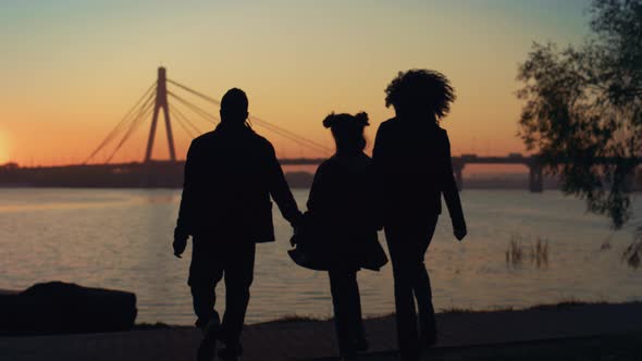 Loving Family Silhouette Walking to River Shore Together at Beautiful Sunset alt