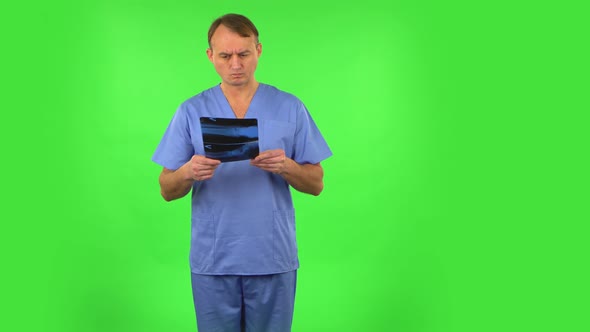 Male Doctor in Blue Coat Reviewing X-ray Pointing on Snapshot. Green Screen alt