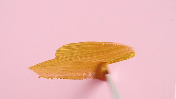 Abstract Brushstrokes of Gold Paint Brush Applied Isolated on a Pink Background alt