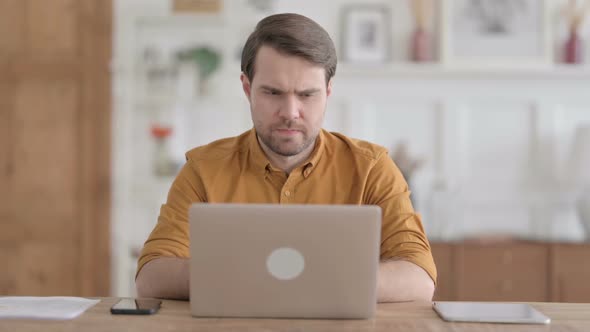 Young Man Thinking while Working on Laptop in Office alt
