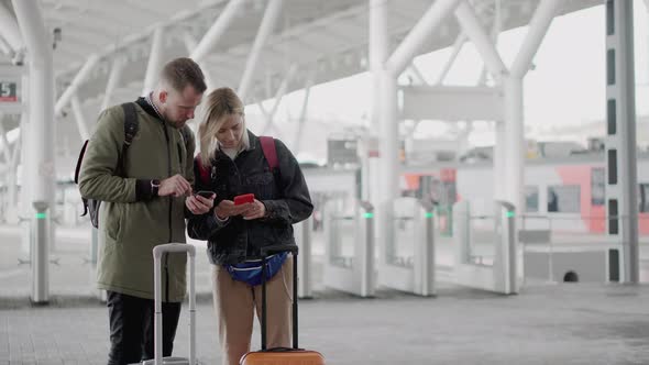 Two Passengers Are Using Smartphones Standing on Platform of Railway Station alt