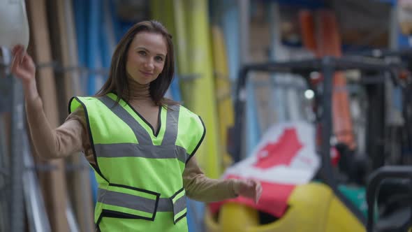 Young Canadian Warehouse Worker Taking Off Hard Hat Touching Hair Looking at Camera Smiling alt