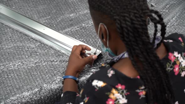 African American woman screwing a screw inside a metal rod on top of bubble wrap. slow motion alt