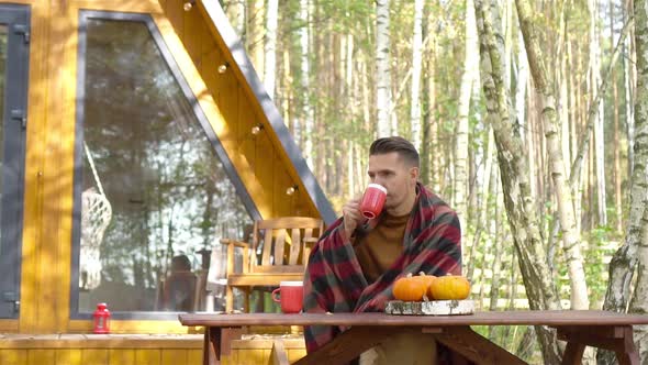 Happy Young Man Drinking Coffee Sitting at the Wooden Table Outdoors