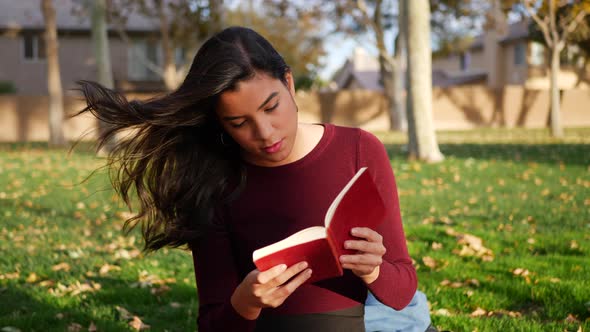 A young woman college student studying and reading a book on a campus lawn or outdoor park SLOW MOTI alt