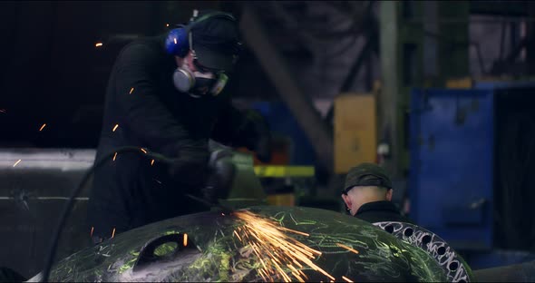 A Professional Worker in a Protective Mask Works with a Grinder in a Factory alt