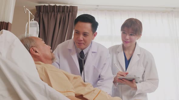 Asian professional doctor and nurse taking care of elderly male patient lying down on bed. alt