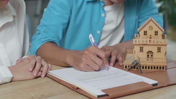 Close Up Of Man'S Hand Signing On House Purchase Contract Paper While Sitting With A Woman alt