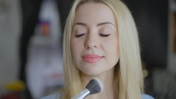 Headshot of Young Confident Gorgeous Blond Woman in Beauty Salon Smiling As Female Hand Applying alt