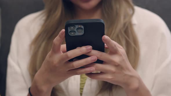 Asian woman in a white shirt sitting on the sofa and using a smartphone.