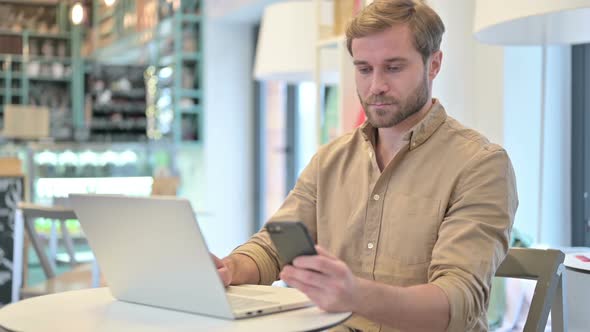 Young Man Using Smartphone and Laptop in Cafe alt
