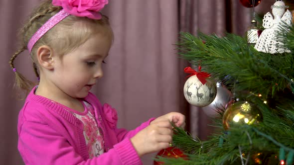 Little Girl Decorates a Christmas Tree. A Child Hangs a Ball on a Christmas Tree Branch. Christmas alt