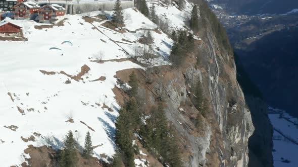 aerial of Paraglider jumping of edge of mountain near beautiful Swiss town - HD crop alt
