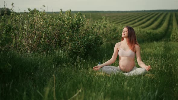 Pregnant young woman with dark hair in a pink top and light pants enjoys the sun outdoors. 