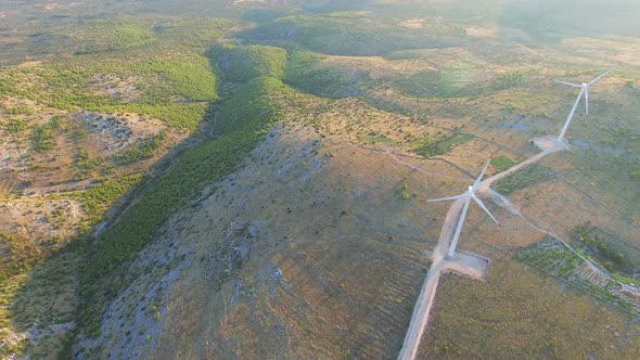 Flying above two elegant white wind turbines on green hills alt