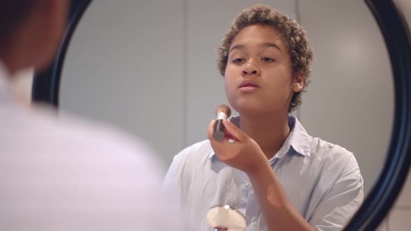 Young African Woman Applying Makeup While Looking in Mirror alt