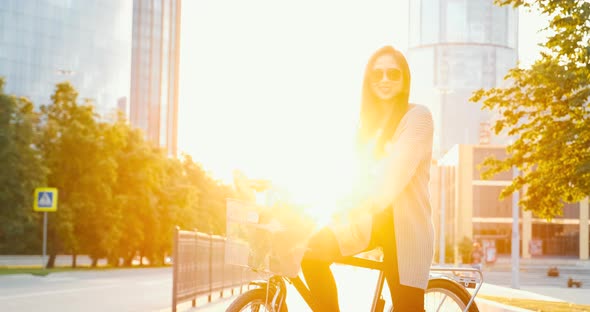 Beautiful girl with classical bike in city at sunset near modern office buildings skyscrapers.