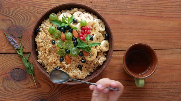 Wholegrain Oatmeal porridge with fresh berries, fruits, nuts, mint leaves in child hands. alt