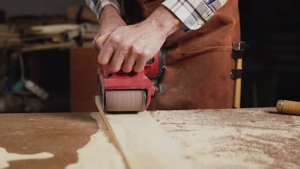 Carpenter Sanding Wood with Belt Sander at Workshop in Wooden Board Project or Woodworking Carpentry alt