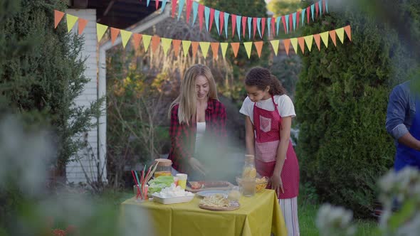 Wide Shot of Caucasian Woman and Mixedrace Teenage Girl Setting Table As African American Man alt