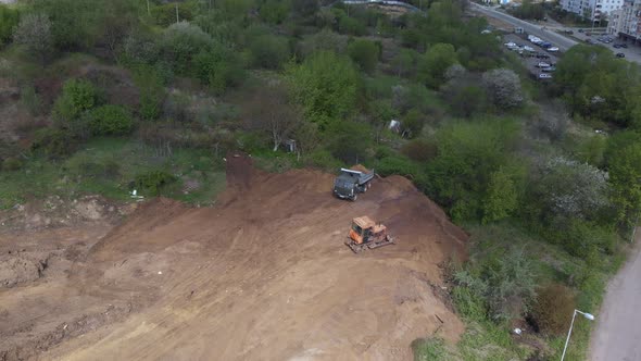 Aerial shot of tipper unloading ground on further construction site.