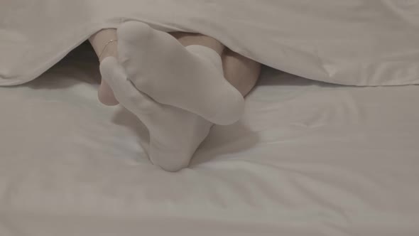 Close Up Shot of Man Laying on Bed with Feet in White Socks and Female Bare Legs Under Blanket in alt