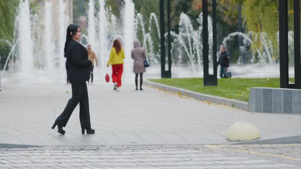 Hispanic Brunette Girl Walks in Park at Lunchtime Walking Slowly Down Street Near the Carriageway on alt
