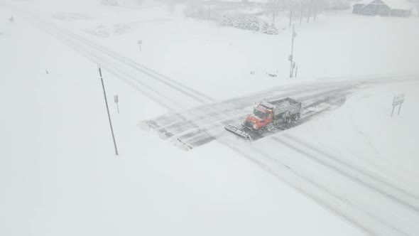 Snowplow clearing highway intersection during snowstorm for rural neighborhood.