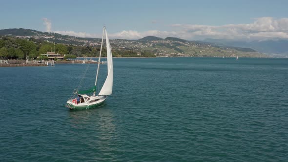Beautiful aerial of boat sailing over lake Geneva and slowly revealing a large city in the backgroun alt
