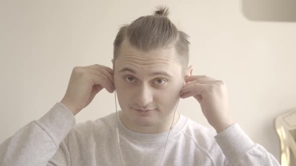 Portrait of Young Caucasian Man Putting on Earphones and Greeting Someone in Video Chat. Close-up of alt