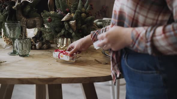 Woman in Plaid Shirt Serving Festive Christmas Table with Small Gift Boxes alt