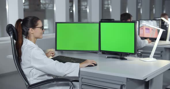 Woman in Lab Coat Sitting at Desktop with Computer in Laboratory alt