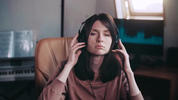A beautiful girl with headphones listens to music in a chair at the computer, dances
