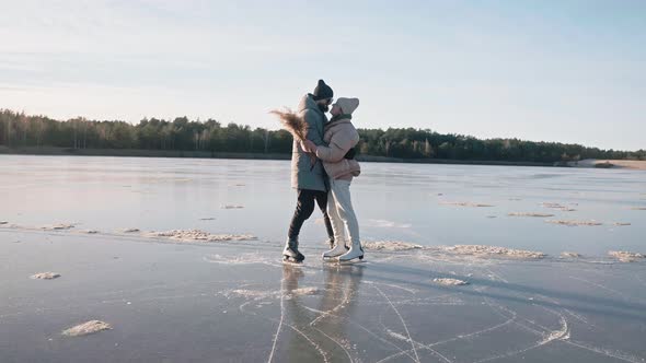 Cute Couple Kisses on a Frozen Lake on a Sunny Winter Day with Nice Landscape